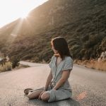 A woman sitting on a coastal road in Antalya during sunset, offering a serene landscape view.